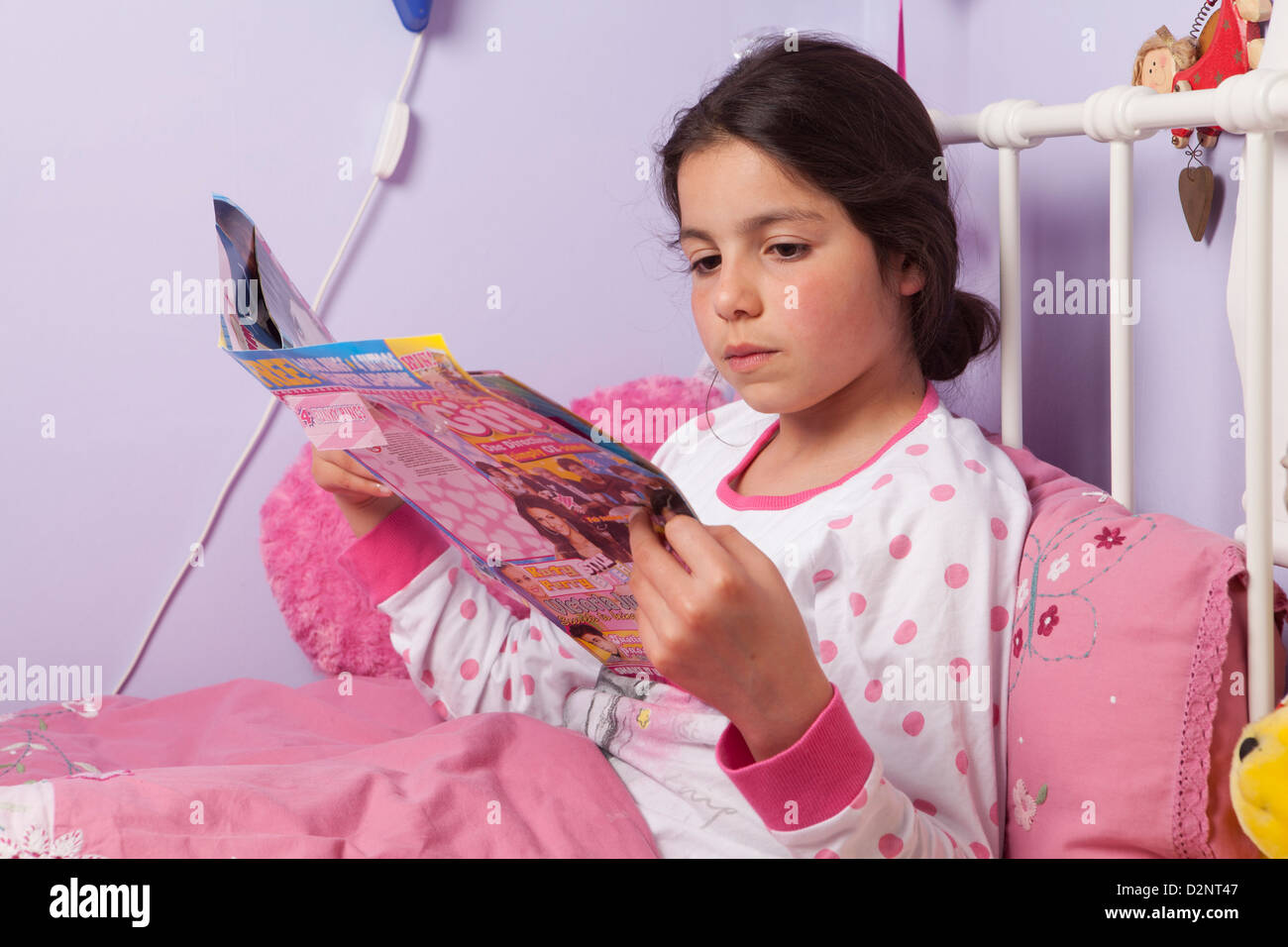 Jeune fille lit un magazine dans son lit Banque D'Images