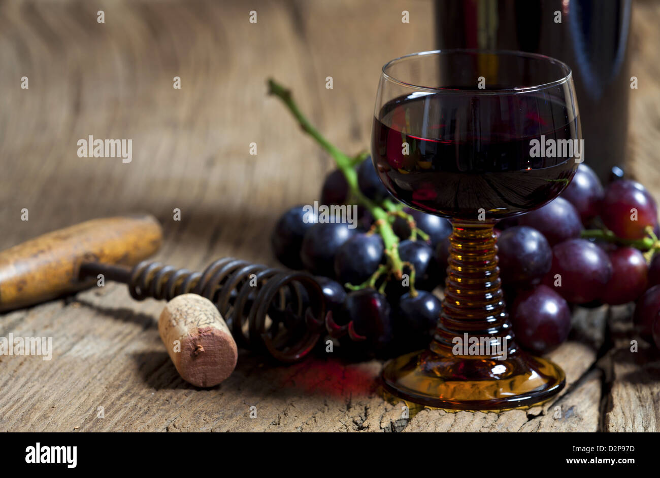 Un verre de vin rouge avec une bouteille et les raisins sont sur une vieille table en bois rustique Banque D'Images