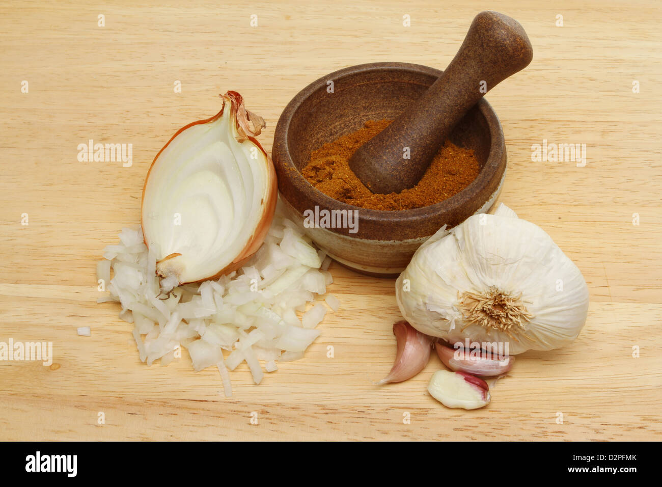 L'oignon, l'ail et le curry en poudre dans un mortier et pilon sur une planche en bois Banque D'Images