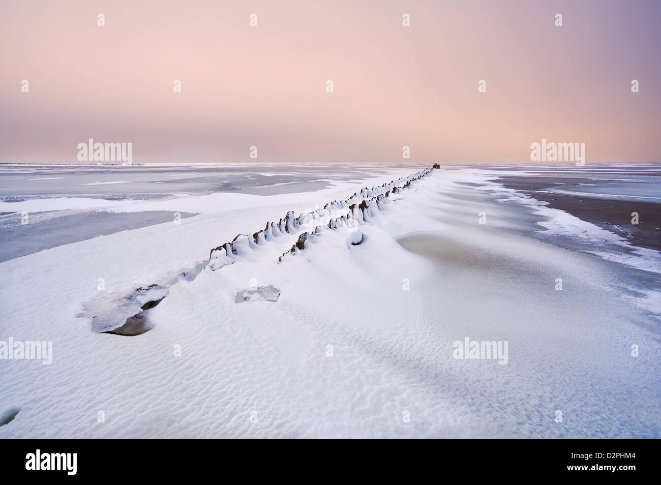 Ancienne digue en mer du Nord gelé sous la neige au coucher du soleil Banque D'Images