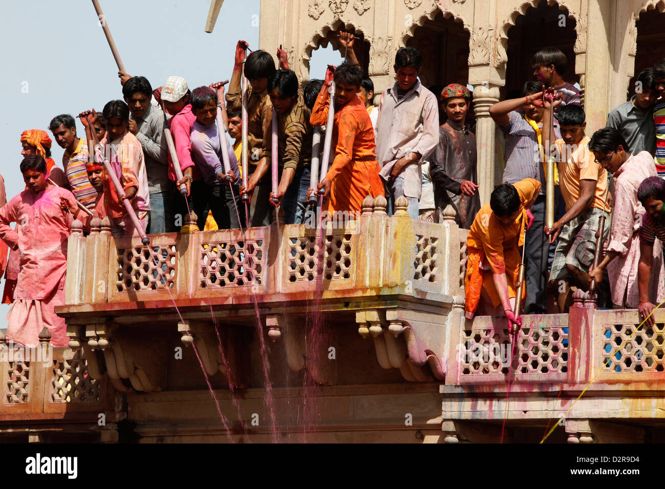Les jeunes hommes célébrant Holi festival par éclaboussures fluides colorés sur les visiteurs du temple, Nandgaon, Uttar Pradesh, Inde, Asie Banque D'Images
