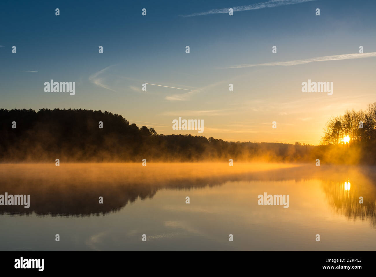 Le soleil n'est qu'à venir plus de West Point Lake, brillant à travers les arbres et se reflète sur l'eau. Ses rayons orange allume le brouillard tôt le matin. L'horizon est légèrement en dessous du centre de l'image en insistant sur le ciel. Banque D'Images