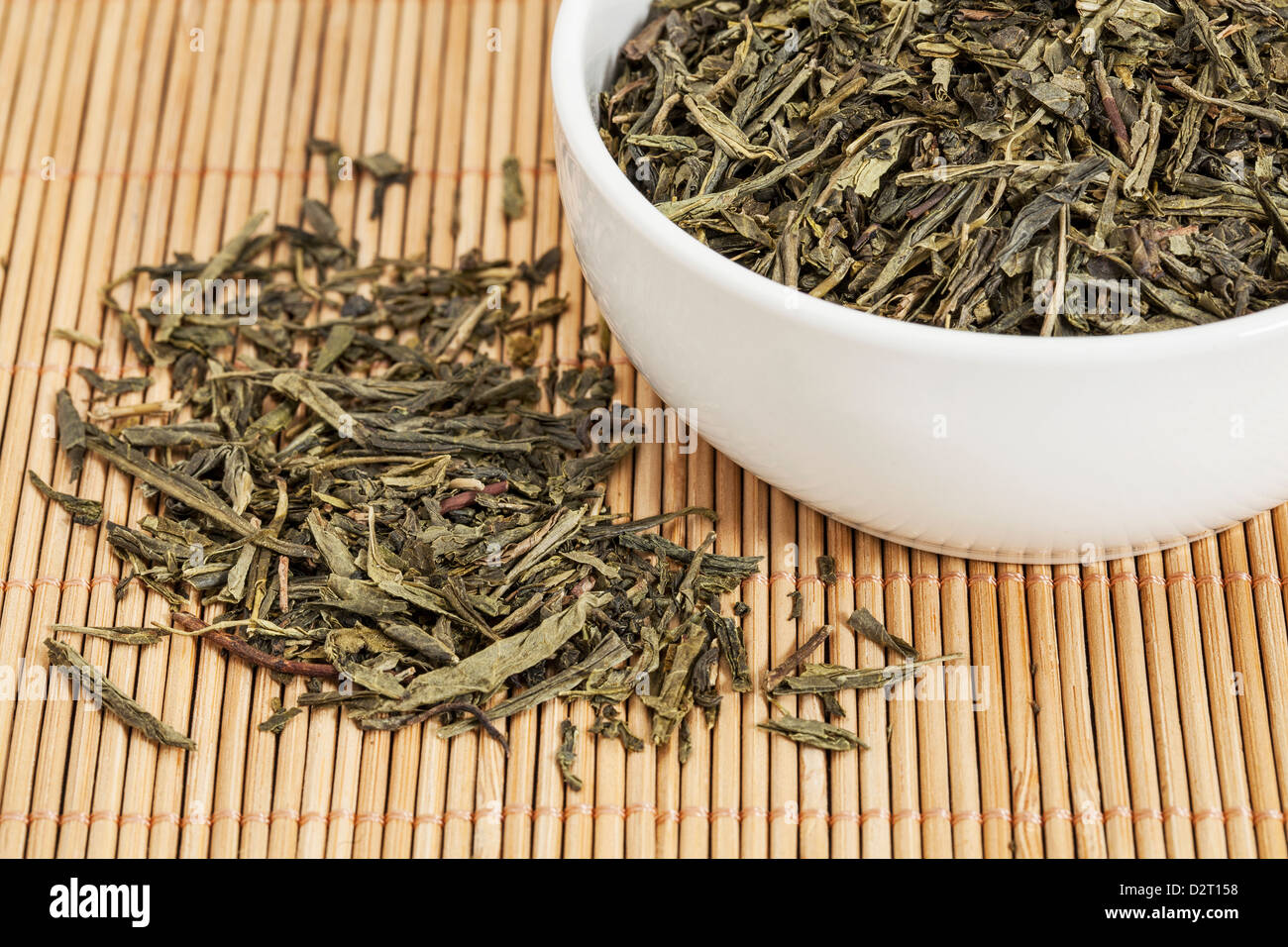 Thé vert Sencha en feuilles dans un livre blanc la chine tasse et renversé sur le tapis de bambou Banque D'Images Thé vert Sencha en feuilles dans un livre blanc la chine tasse et renversé sur le tapis de bambou Banque D'Images