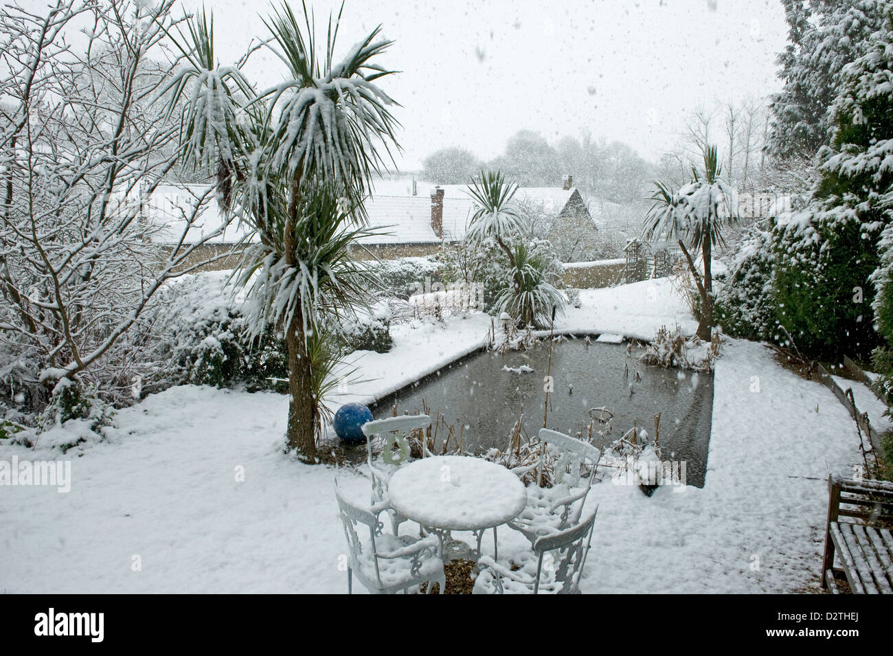 Étang de jardin, table, chaises et d'arbustes dans une forte tempête de neige, le Devon, Banque D'Images