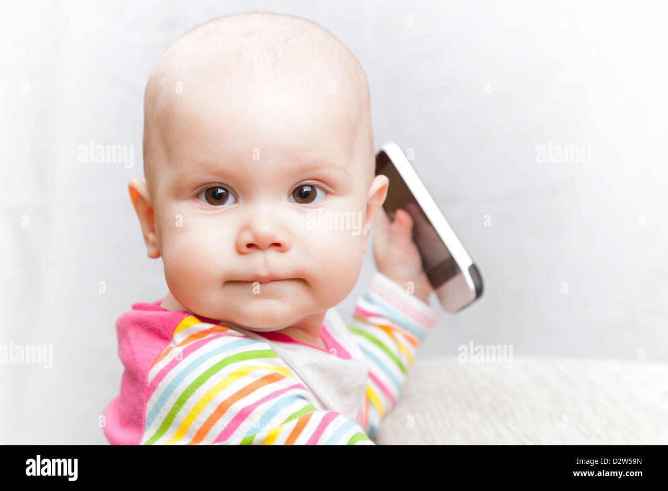 Petit bébé dans des vêtements à rayures occasionnels joue avec un téléphone mobile Banque D'Images