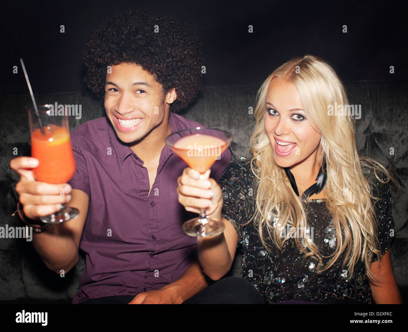 Portrait of enthusiastic couple toasting cocktails in nightclub Banque D'Images