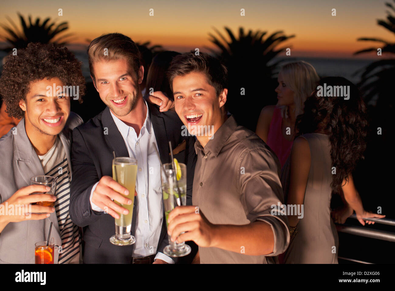 Portrait of smiling men toasting cocktails sur balcon au coucher du soleil Banque D'Images