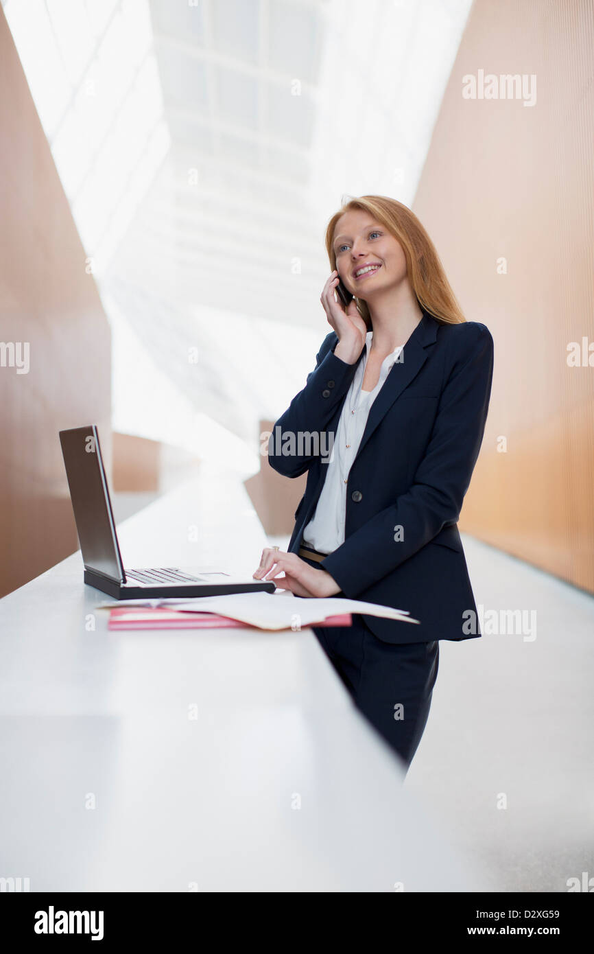 Smiling businesswoman talking on cell phone and using laptop in office Banque D'Images