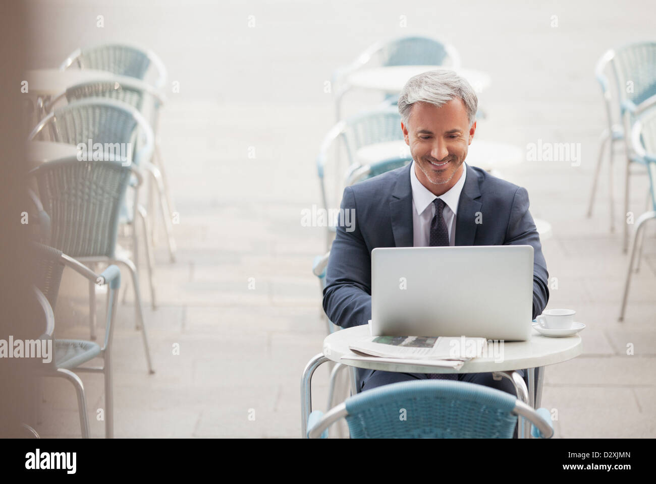 Smiling businessman using laptop at sidewalk cafe Banque D'Images