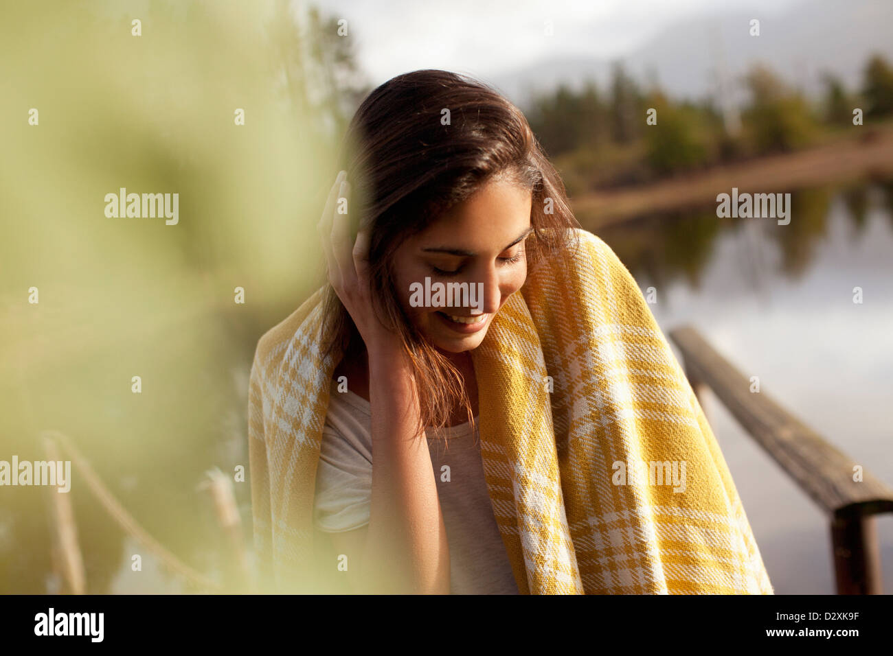 Smiling woman wrapped in blanket at lakeside Banque D'Images