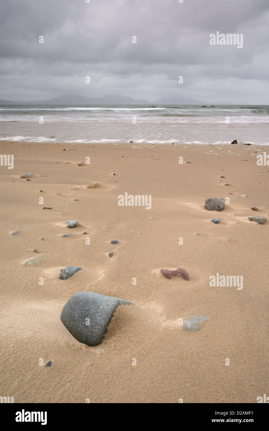 Rochers éparpillés le long de la plage de Newborough, Anglesey, à marée montante. Banque D'Images