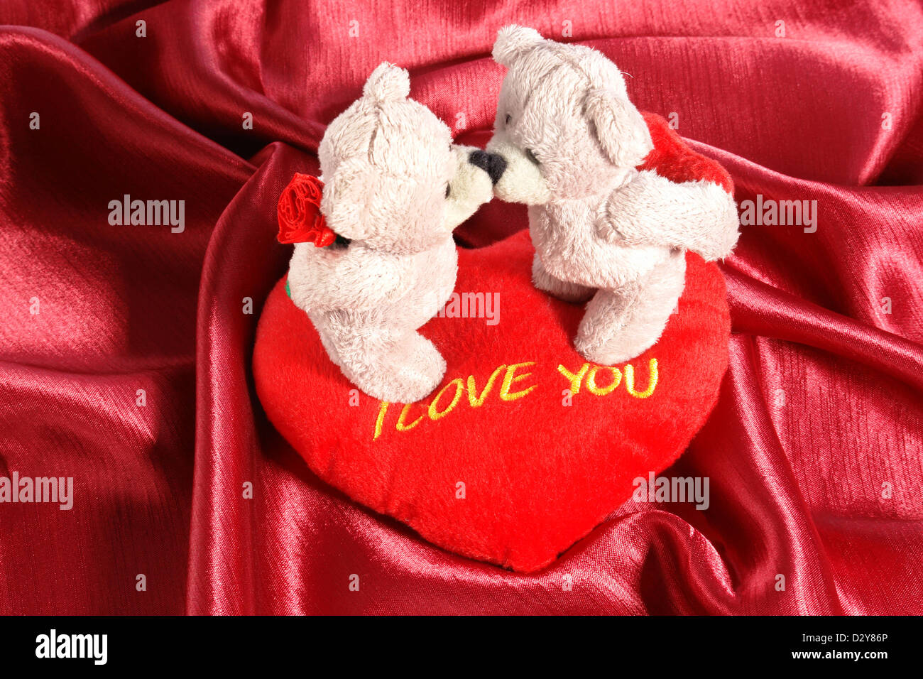 Deux oursons en peluche qui s'embrassent sur l'oreiller en forme de cœur en peluche sur tissu cramoisi Banque D'Images