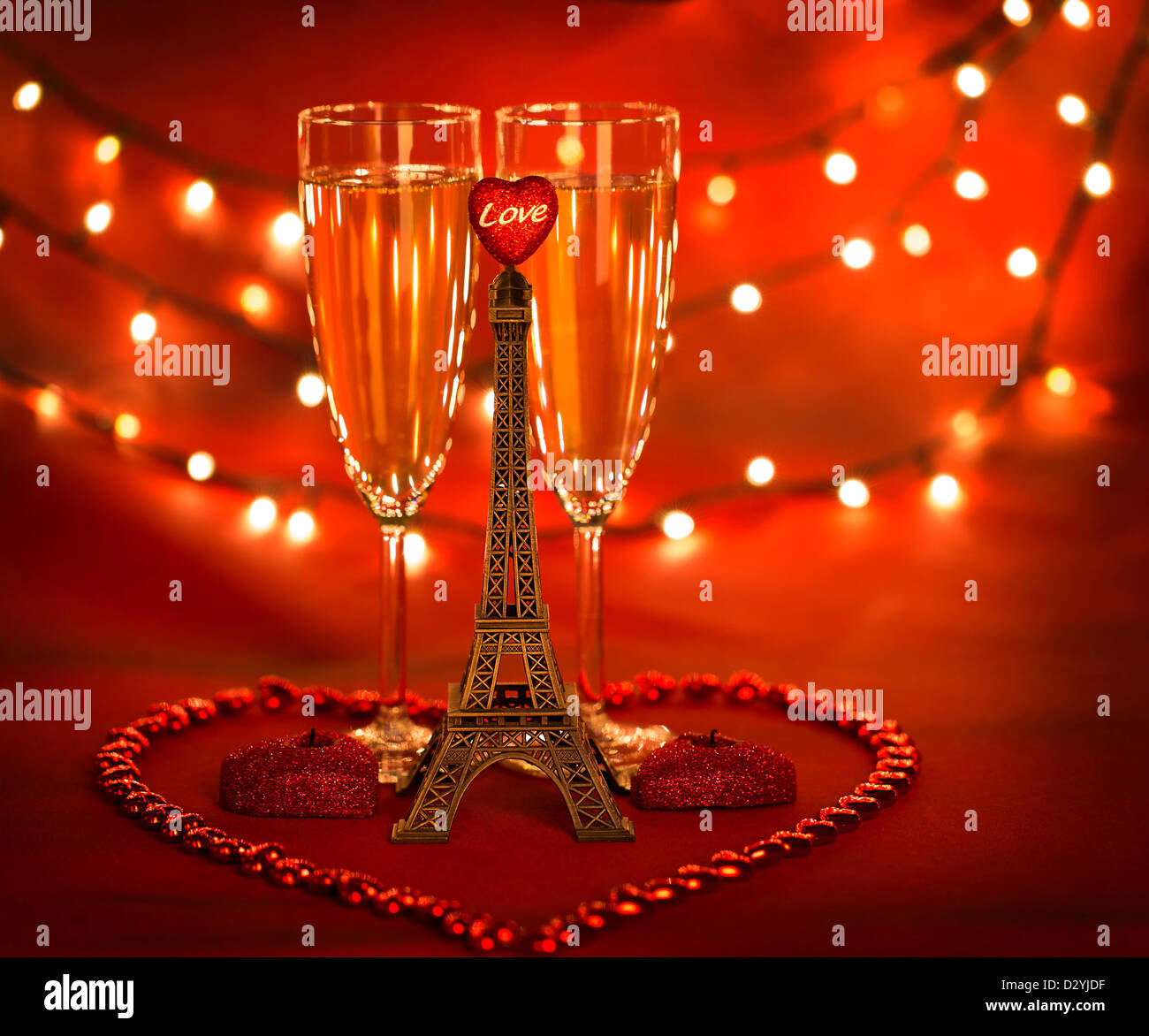 Photo de deux verre à champagne décorées avec peu de Tour Eiffel et de bougies en forme de cœur et des perles sur fond rouge Banque D'Images