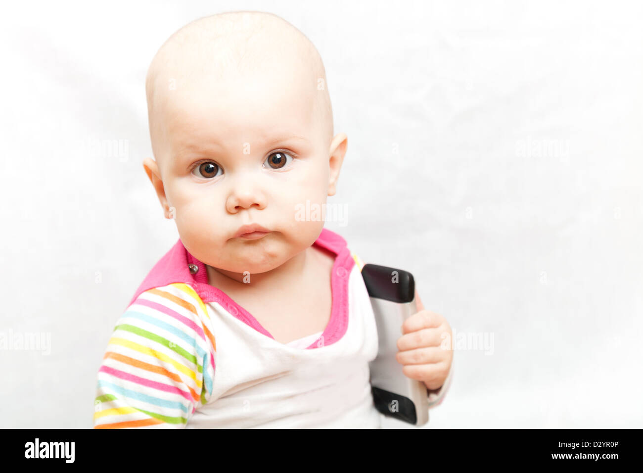 Petit bébé dans des vêtements à rayures occasionnels joue avec un téléphone mobile Banque D'Images