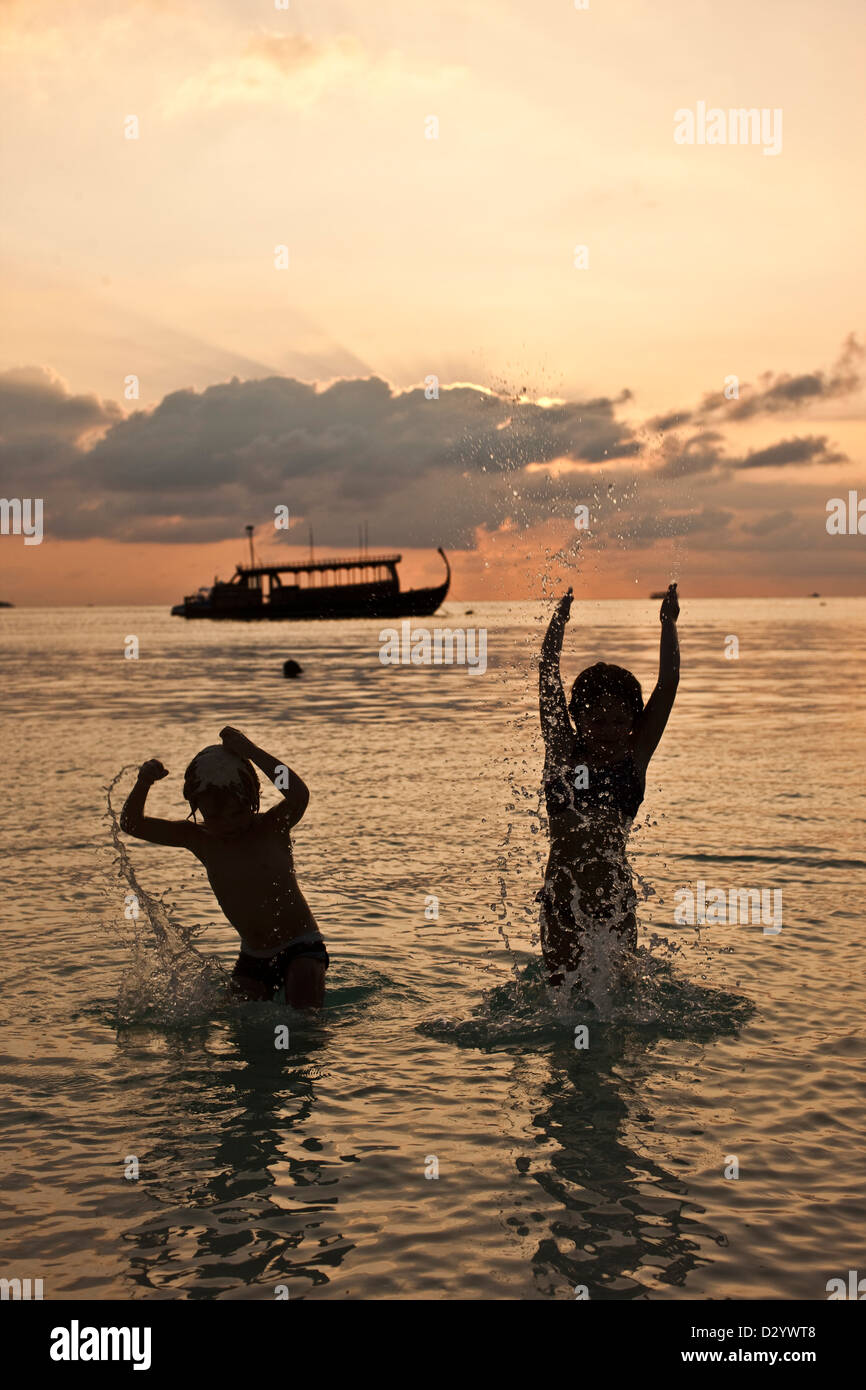 Éclaboussures des enfants à bord de l'eau, coucher de soleil sur Kuda Hura, Maldives Banque D'Images