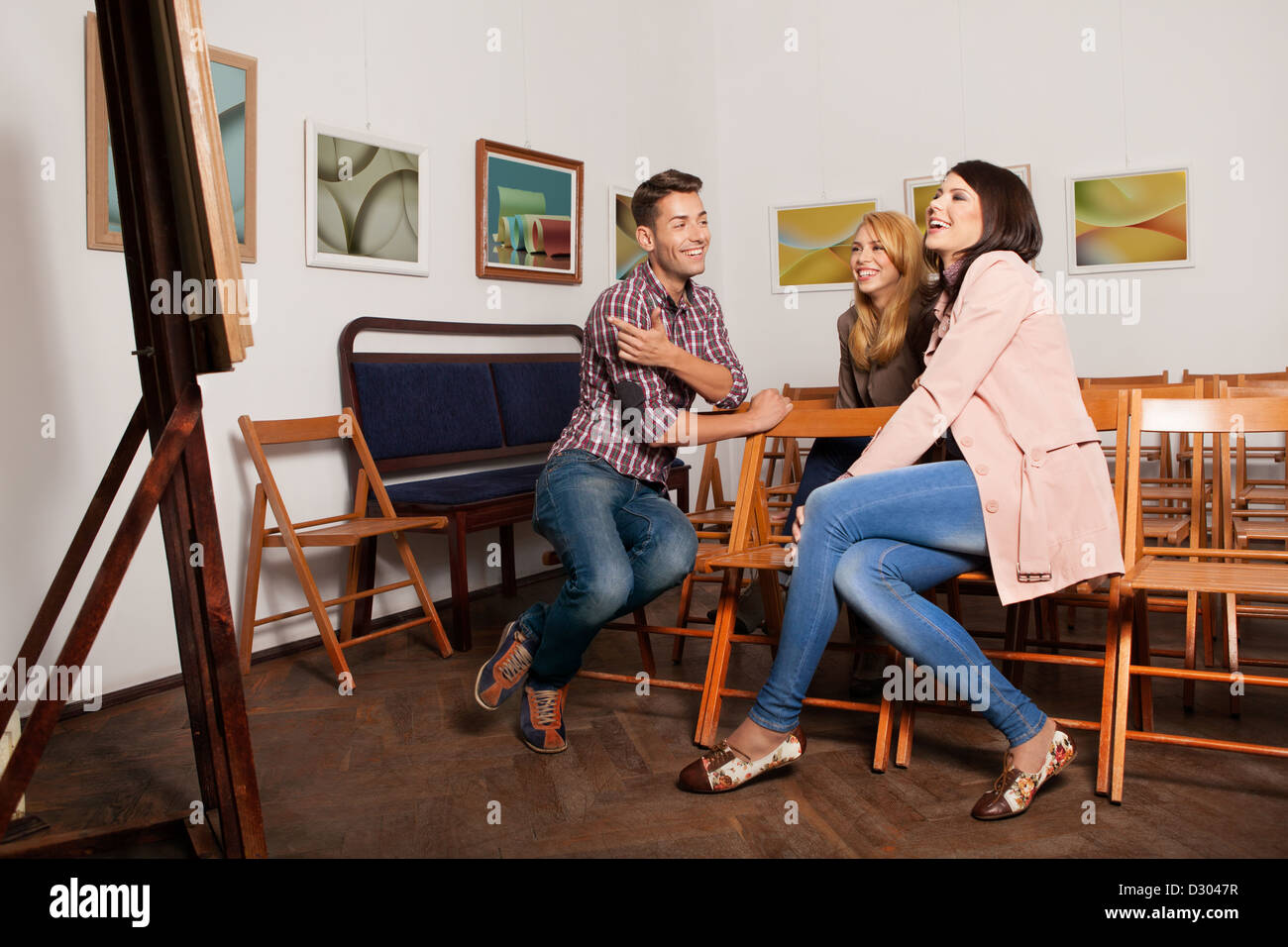 Les jeunes à la bonne personnes lors d'une exposition de photographie de s'asseoir sur des chaises en bois, riant et pointig vers une œuvre d'art. Banque D'Images