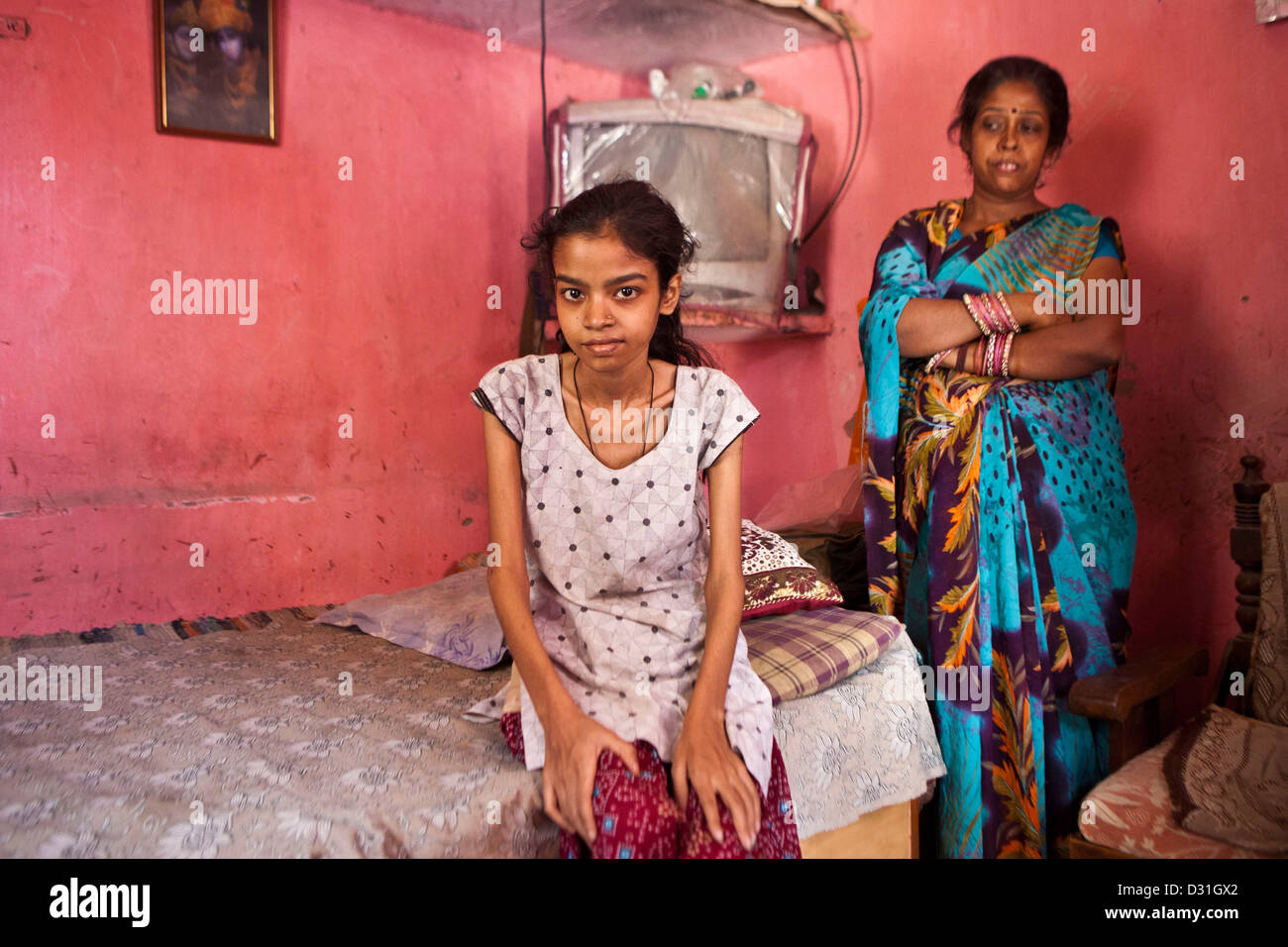Une jeune femme indienne est assise sur son lit avec sa mère debout derrière elle dans Meethapur slum, Delhi, Inde. Banque D'Images