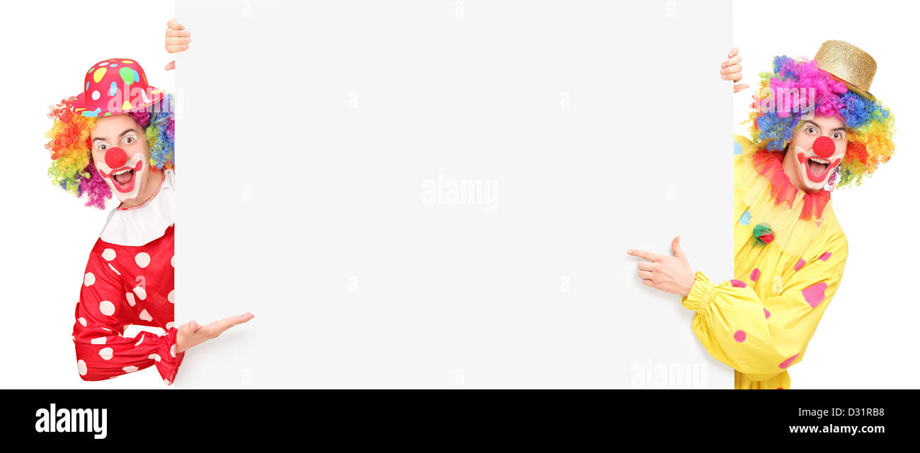 Funny clowns de cirque posant derrière un panneau vierge et faisant des gestes isolés contre fond blanc Banque D'Images
