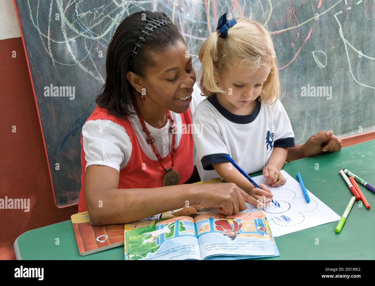 L'encadrement de l'enseignant la fille à attirer et reconnaît les formes à l'extérieur de la région de sunny ecole maternelle playschool Banque D'Images