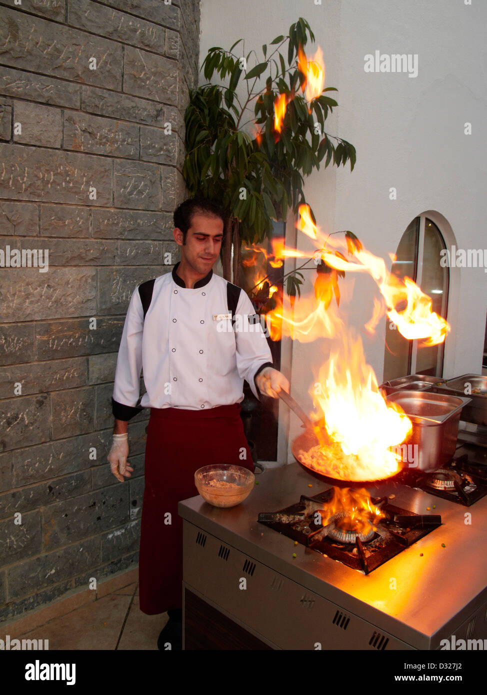 L'huile chaude sur une poêle à frire éclate en flammes tandis que le chef du restaurant prépare un repas sur une cuisinière à gaz extérieure. Village de Torba, péninsule de Bodrum, Turquie. Banque D'Images