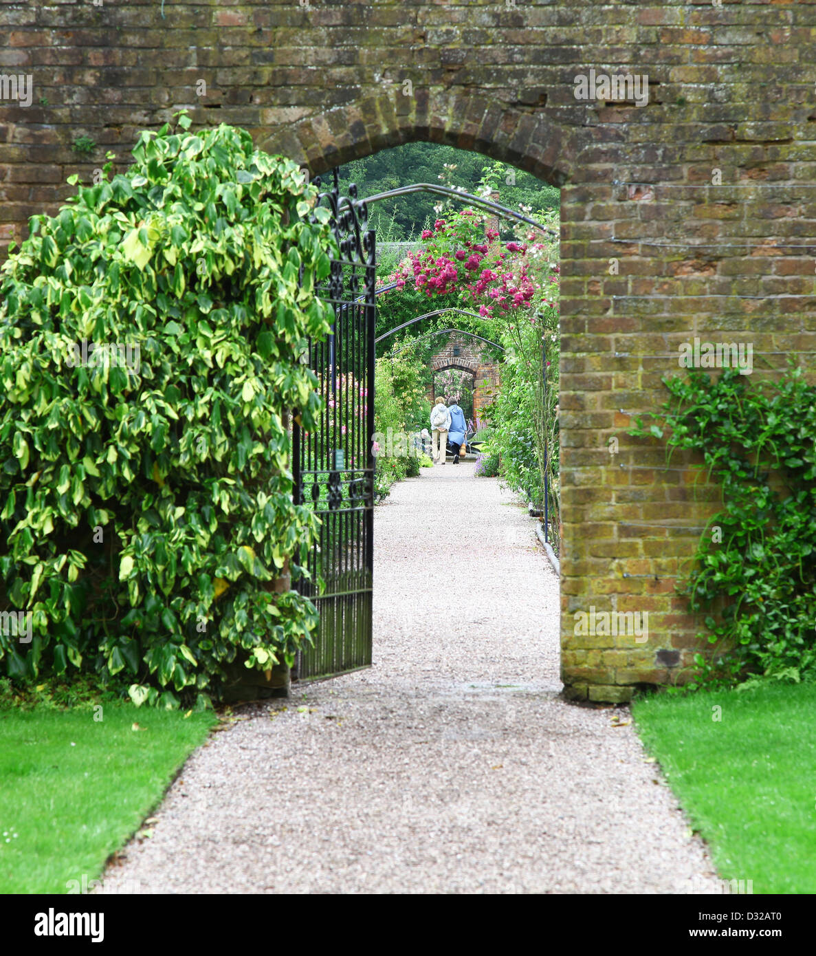 Regarder à travers une grille de fer, dans un mur de briques avec de personnes dans la distance à Arley Hall gardens Cheshire England UK Banque D'Images