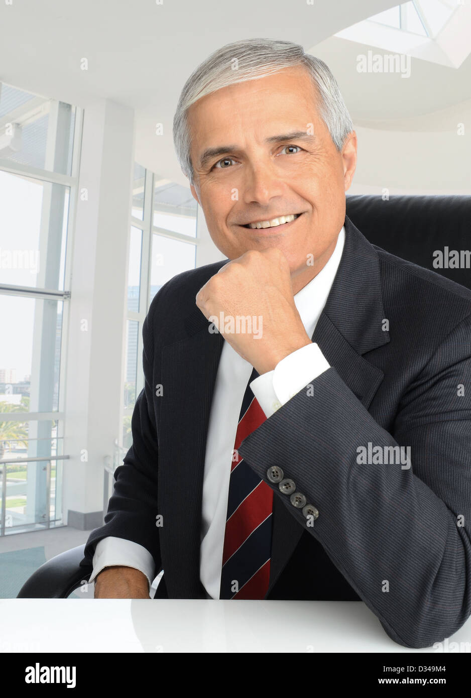 Portrait of a middle aged businessman assis à son bureau avec sa main sur son menton. L'homme est souriant à la caméra. Banque D'Images