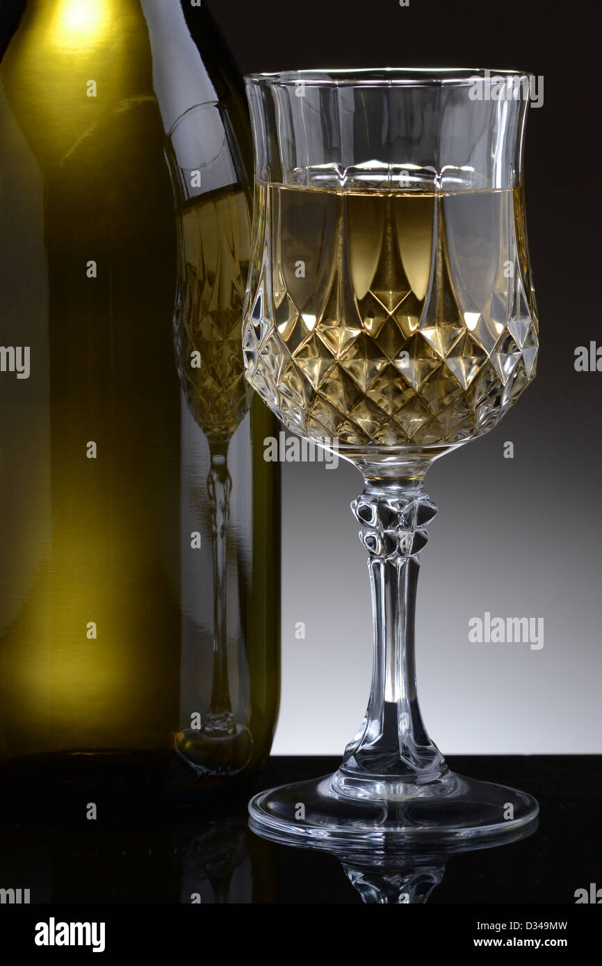 Libre de cristal taillé verre de vin blanc et une bouteille contre une  lumière sur fond gris foncé Photo Stock - Alamy