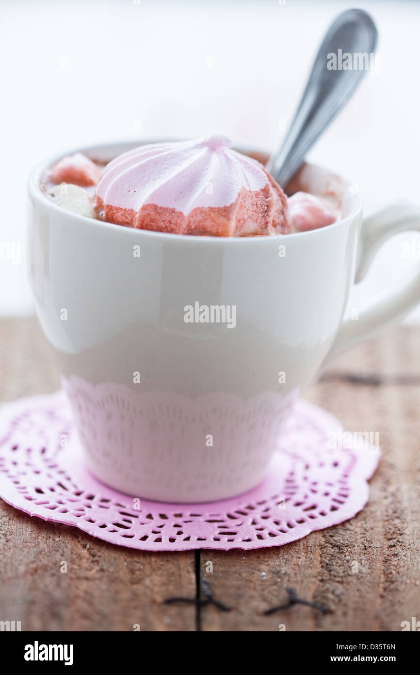 Libre de tasse de chocolat chaud avec une cuillère de meringue rose et reposant sur de petits tapis de table rose sur table en bois Banque D'Images