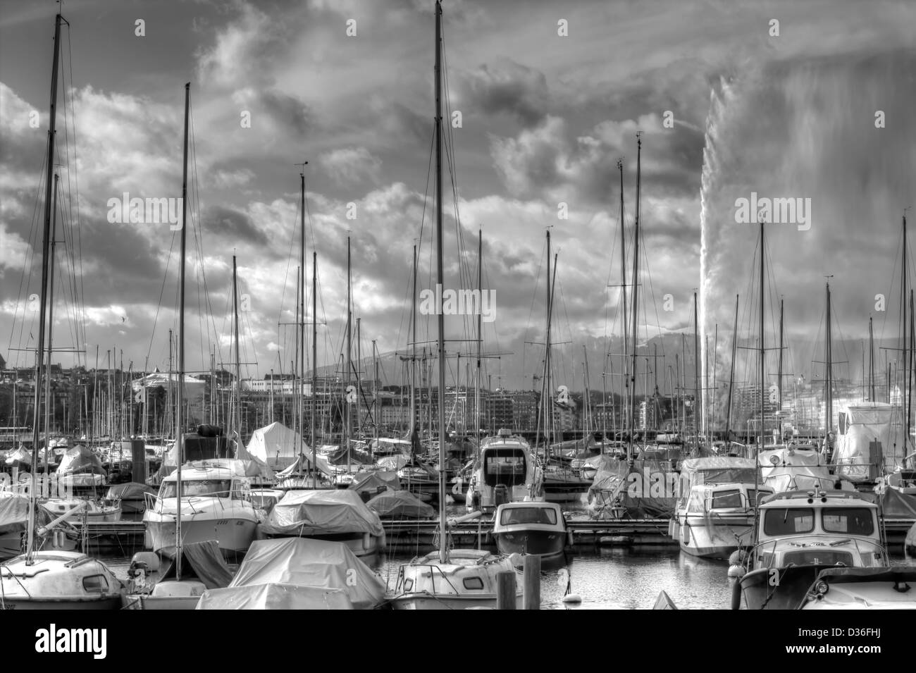 Yachts à côté de centre-ville de Genève avec fontaine, montagnes et ciel nuageux sur l'arrière-plan à jour ensoleillé. Noir et blanc. Banque D'Images