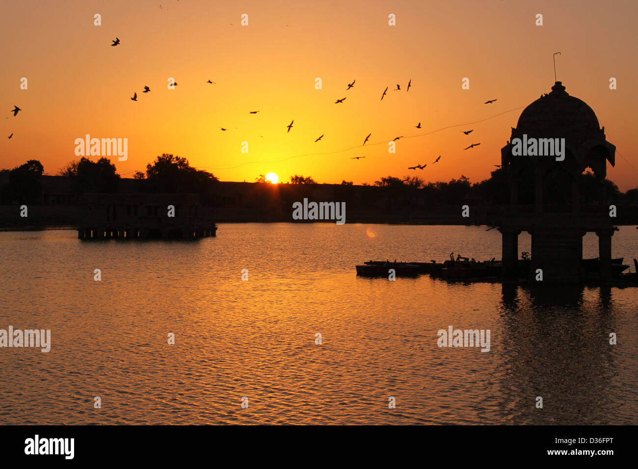 Lever du soleil à Gadi Sagar Lake avec silhouette d'un dôme au milieu et les oiseaux voler, le Rajasthan en Inde Banque D'Images