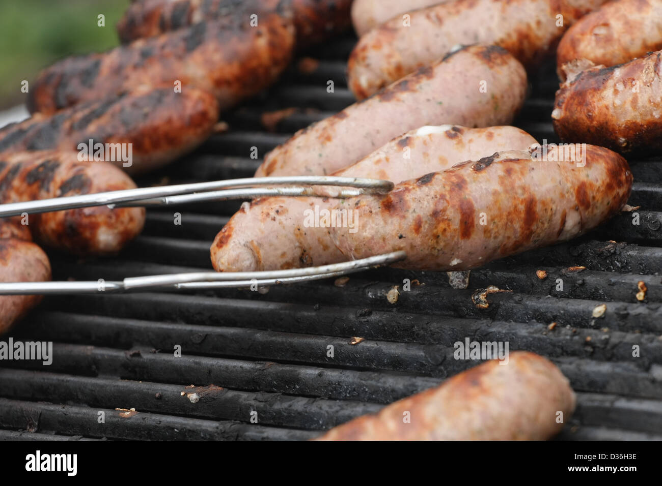 En dehors de la cuisson des saucisses sur un barbecue d'être tourné à l'aide de pinces Banque D'Images