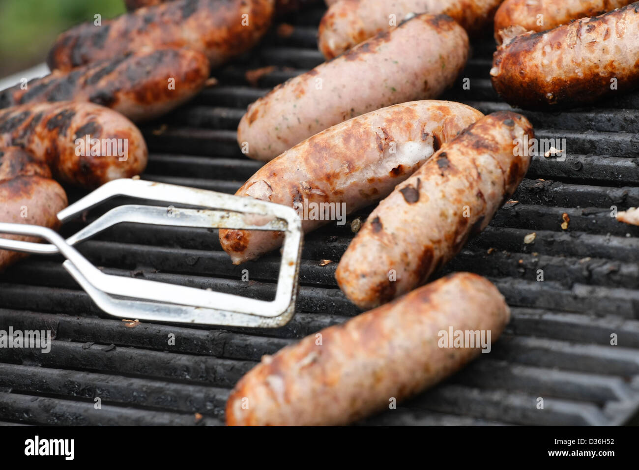 En dehors de la cuisson des saucisses sur un barbecue d'être tourné à l'aide de pinces Banque D'Images