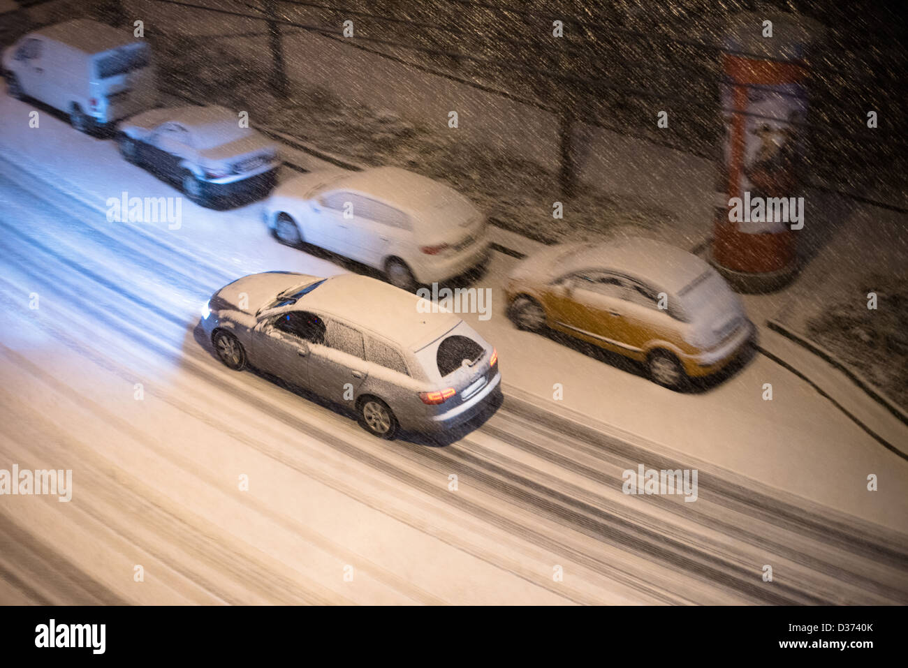 Vue de dessus sur les voitures garées le long d'une rue et une voiture conduite de nuit dans la neige de l'hiver Banque D'Images