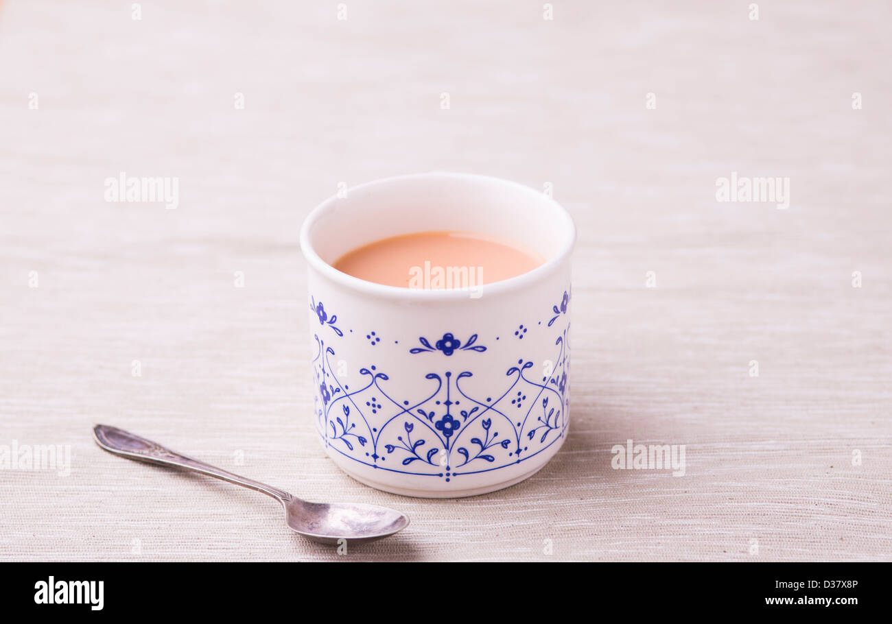 Tasse de Rooibos (buisson rouge) Thé au lait dans un service à la Chine avec une cuillère ancienne sur un fond neutre. Banque D'Images