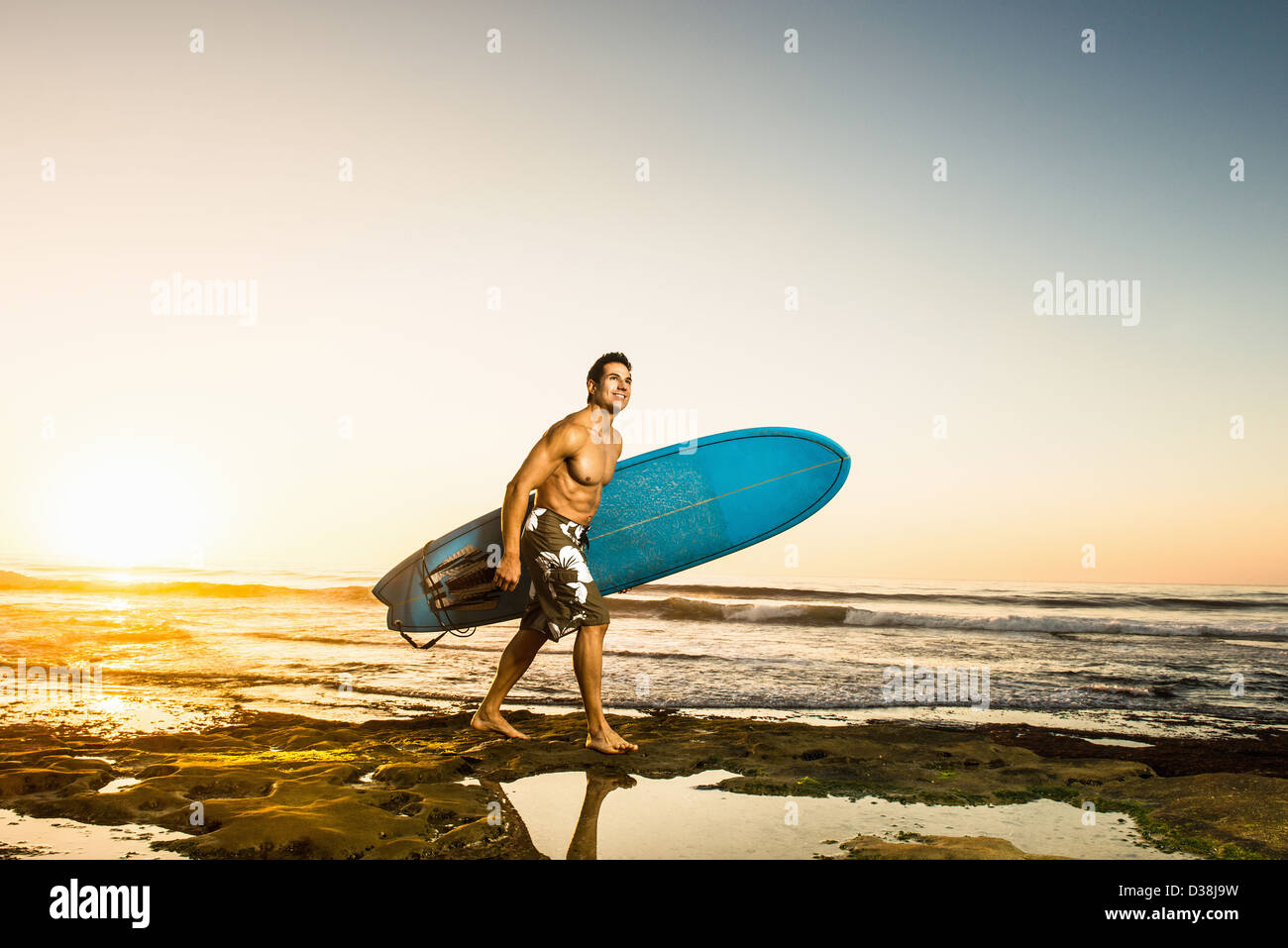 Man carrying surfboard on Rocky beach Banque D'Images