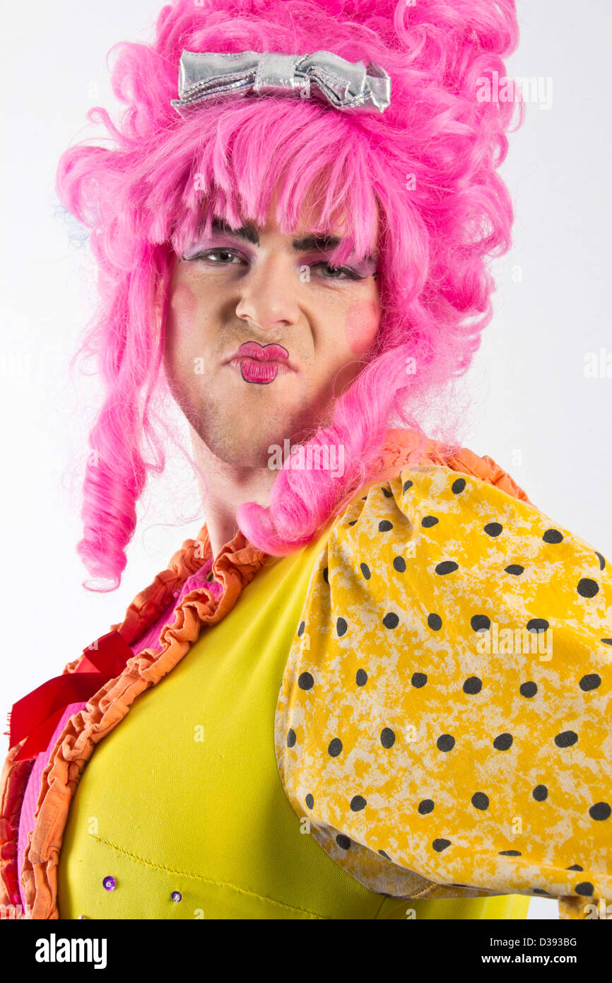 L'homme habillé en femme Panto Dame moues pour l'appareil photo avec la perruque rose et jaune robe à pois. Banque D'Images