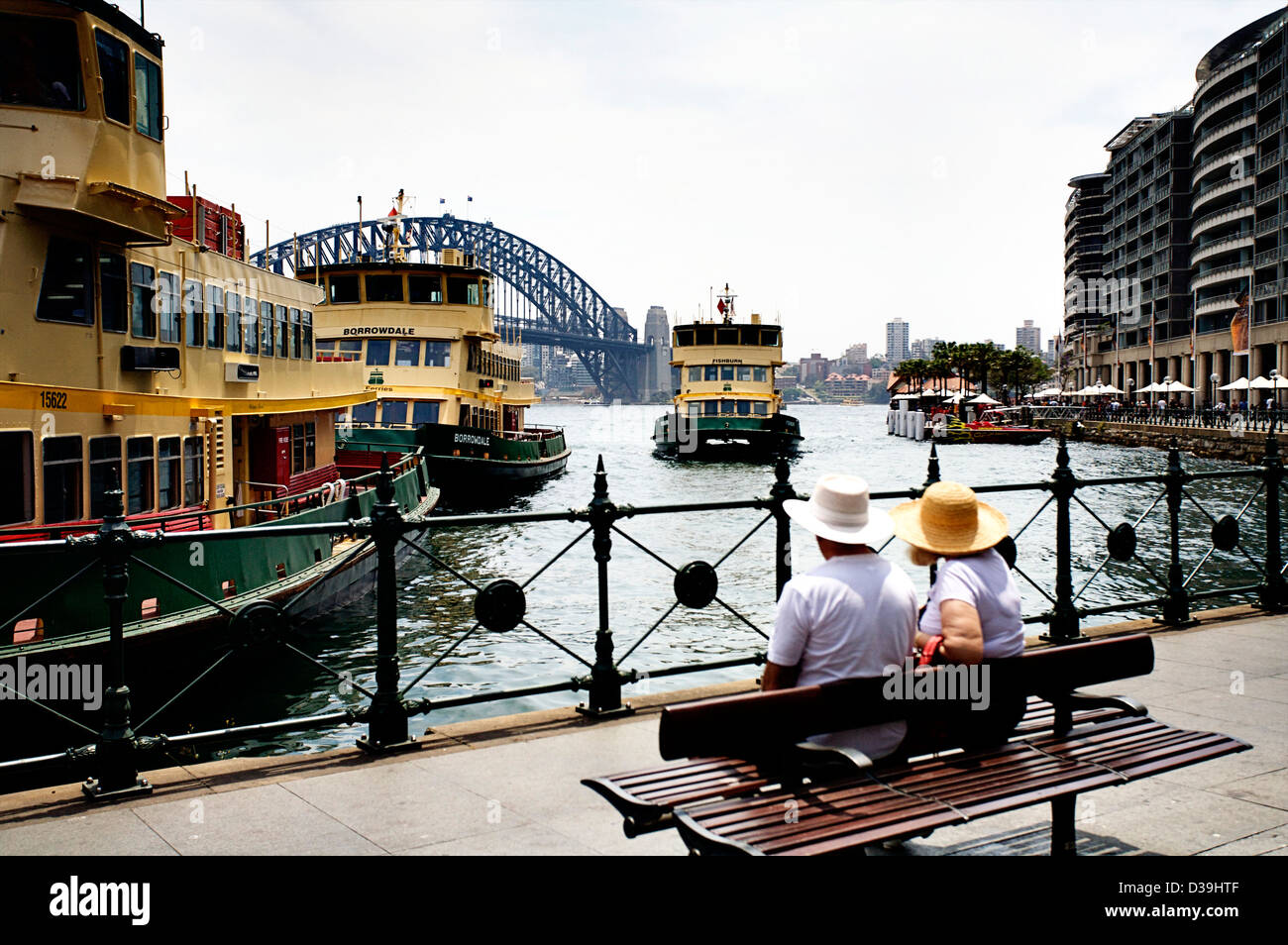 Un couple assis sur un banc public regardant un quai 'Sydney Ferry' à Circular Quay, à Sydney, Nouvelle-Galles du Sud, Australie. Banque D'Images