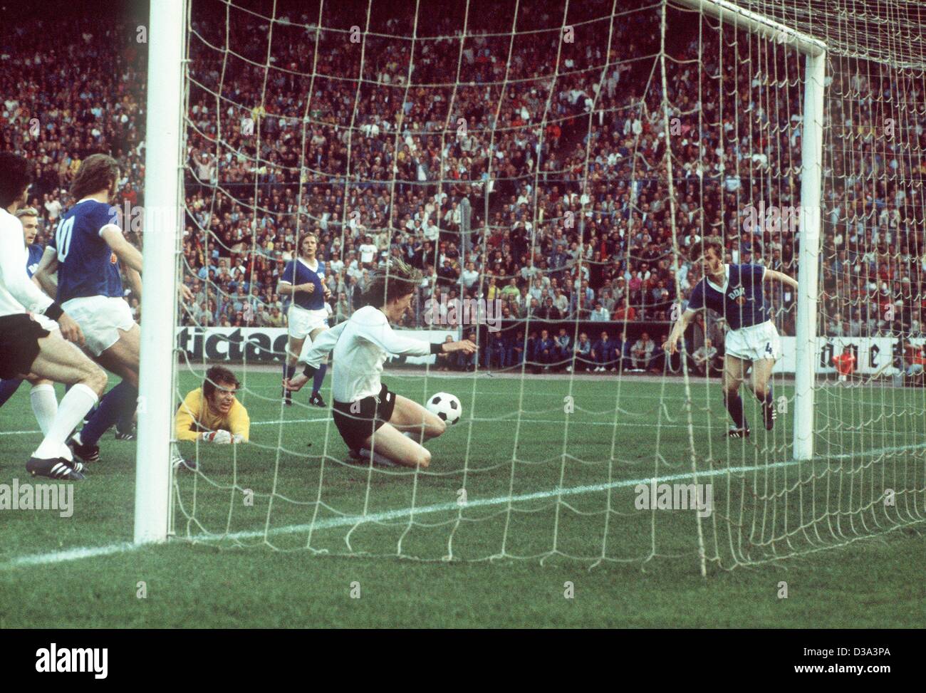 (Afp) - l'est le gardien de but Allemand Jürgen Croy (tricot jaune) se trouve sur le sol tandis que l'attaquant de l'Allemagne de l'Ouest Jürgen Grabowski (C) passe à côté de l'objectif pendant la Coupe du Monde de football match RFA et RDA à Hambourg, le 22 juin 1974. GDR defender Konrad Weise (R) regarde la scène. Le jeu terminé 1:0 pour le Ge Banque D'Images