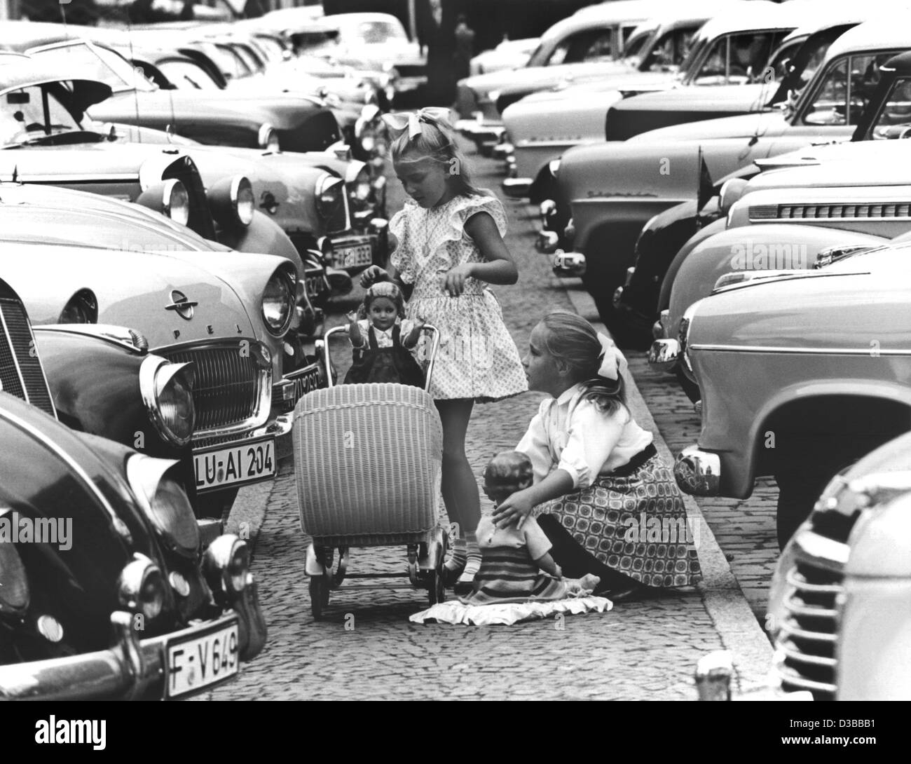 (Afp) - Deux petites filles jouent avec leurs poupées dans l'espace entre les voitures en stationnement pendant leurs vacances d'été à Francfort, 22 juillet 1957. Banque D'Images