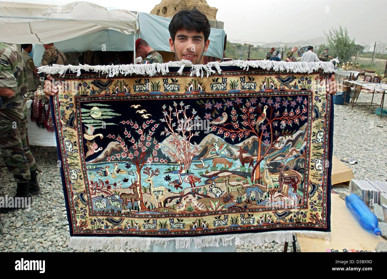 (Afp) - Un vendeur montre un tapis à la vente à proximité du marché aux puces près de l'aéroport de Kaboul, Afghanistan, 3 août 2003. Sur le marché hebdomadaire tout sur les tapis et bijoux à des copies pirates de CD et DVD est disponible. Banque D'Images