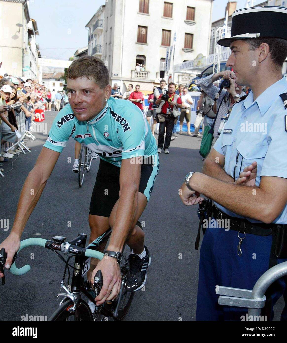 (Afp) - vainqueur Olympique Allemand Jan Ullrich (Team Bianchi) chevauche son vélo au-delà d'un agent de police français vers la ligne de départ de la 14e étape du Tour de France à Saint-Girons, France, 20 juillet 2003. La 14e étape s'étend sur une distance de 191,5 kilomètres de la ville française de Saint-Girons à Loudenvielle-Le Louron. C'est la première de trois étapes qui conduisent l'ensemble des Pyrénées. Banque D'Images