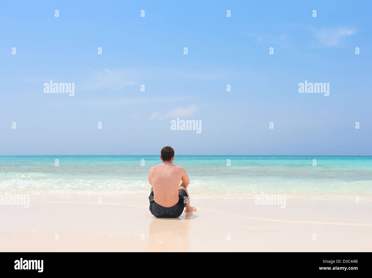 Jeune homme assis seul sur une plage tropicale de l'archipel de Los Roques, Venezuela Banque D'Images