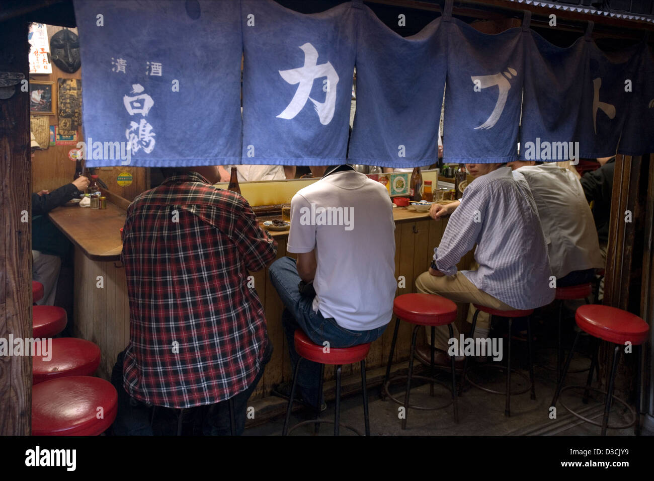 Les clients derrière un rideau noren profitez de la bonne nourriture et de l'amitié au comptoir eatery restaurant à Omoide Yokocho, Memory Lane, Tokyo Banque D'Images