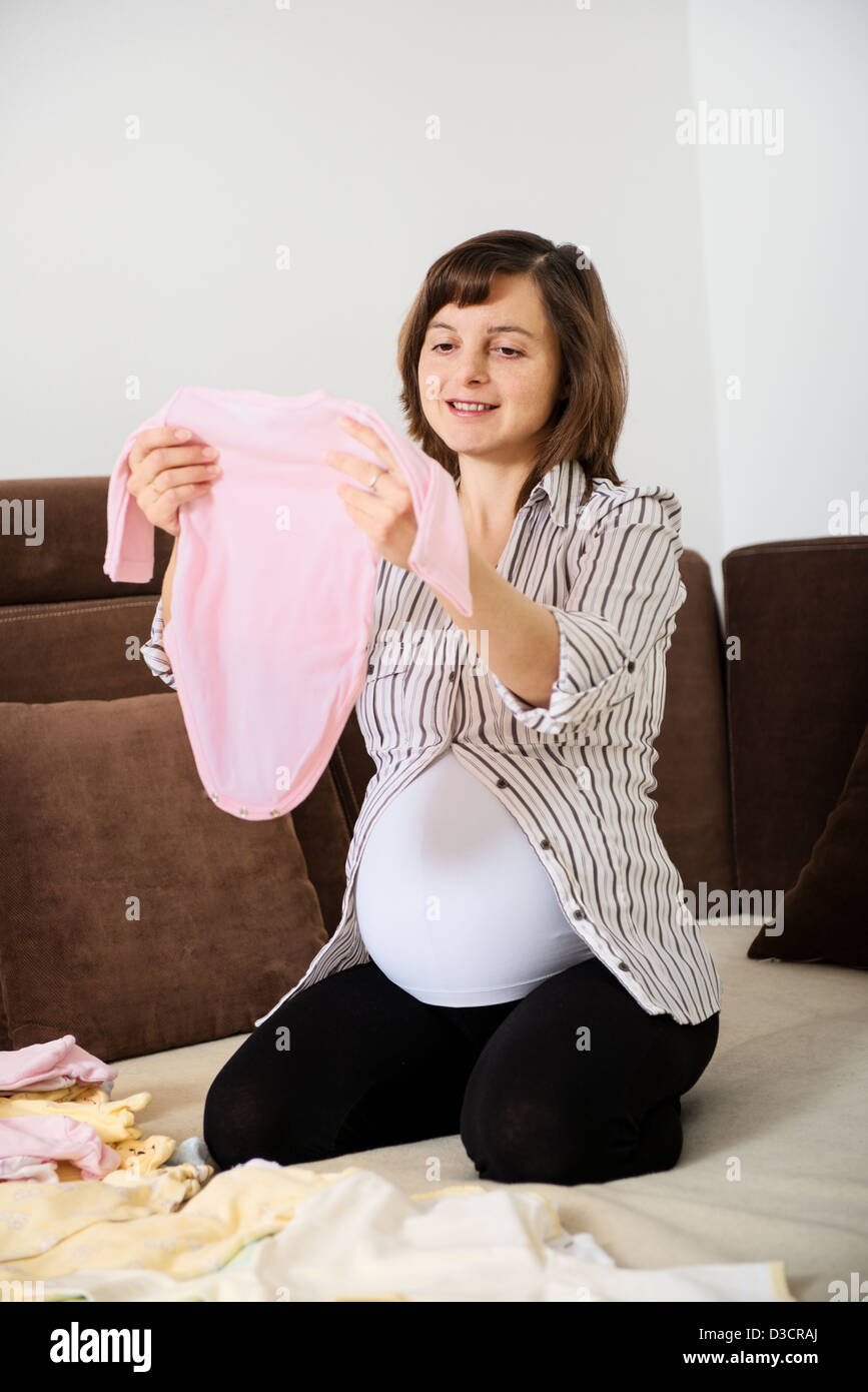 Femme enceinte la préparation de vêtements de bébé à la maison sur canapé Banque D'Images