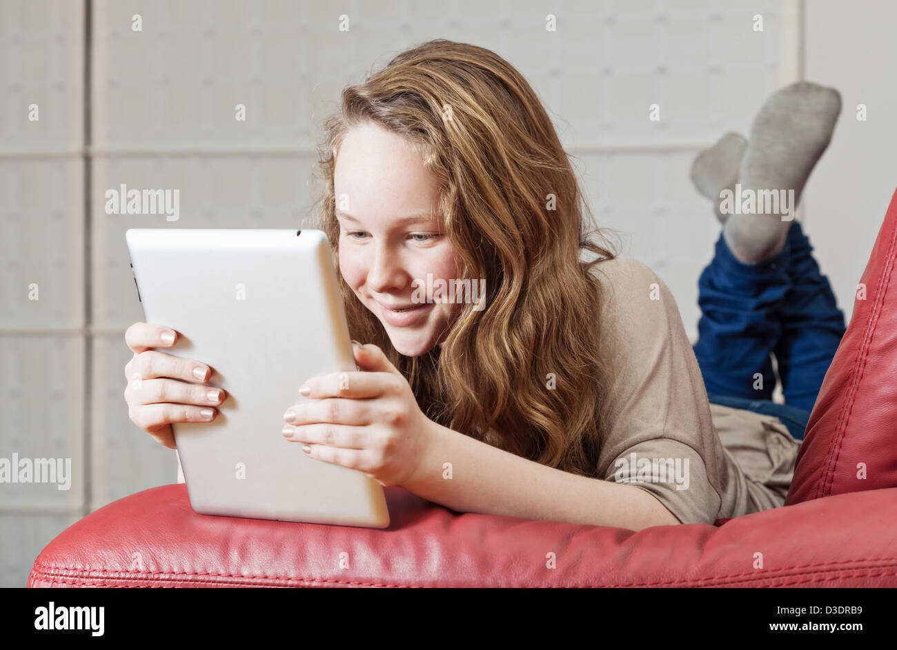 Smiling adolescent girl lying on sofa with tablet computer Banque D'Images