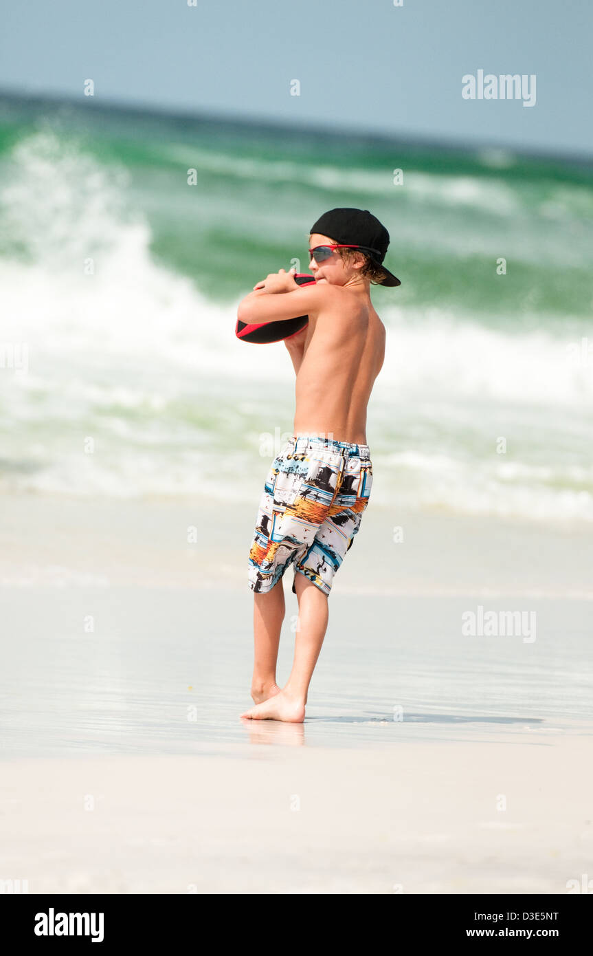 Jeune garçon en maillot de bain à jouer au football à la plage avec l'océan  en arrière-plan Photo Stock - Alamy