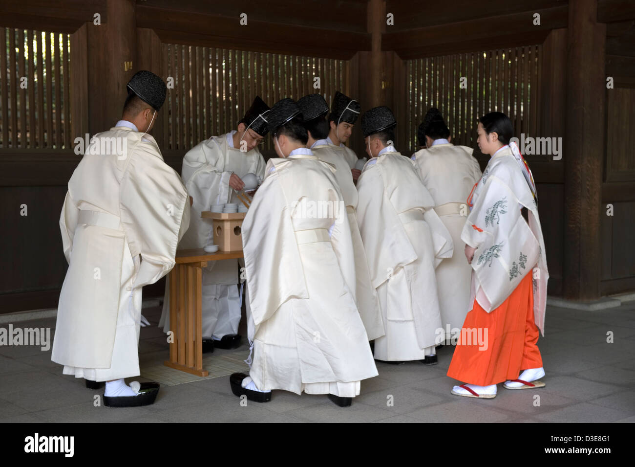 Les prêtres Shinto et une jeune fille en robe rouge miko prendre part au plaisir de boire le rituel religieux cérémonie à Meiji Jingu, Tokyo, Japon. Banque D'Images