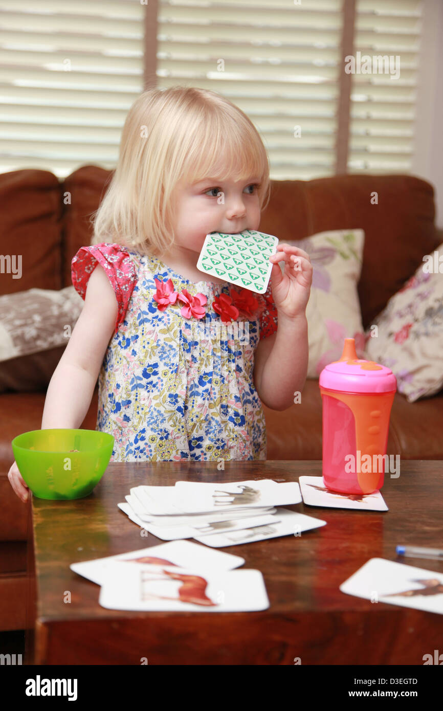 Bébé fille un verre d'un bécher et une collation tout en jouant à l'intérieur. Banque D'Images