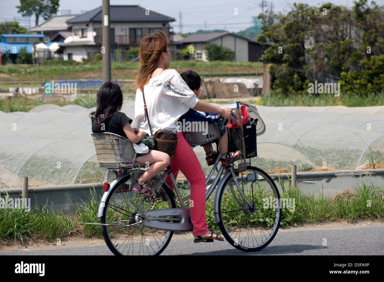 Mère à travers la préfecture de Kanagawa campagne sur un vélo avec son fils et sa fille à bord dans des sièges avant et arrière. Banque D'Images