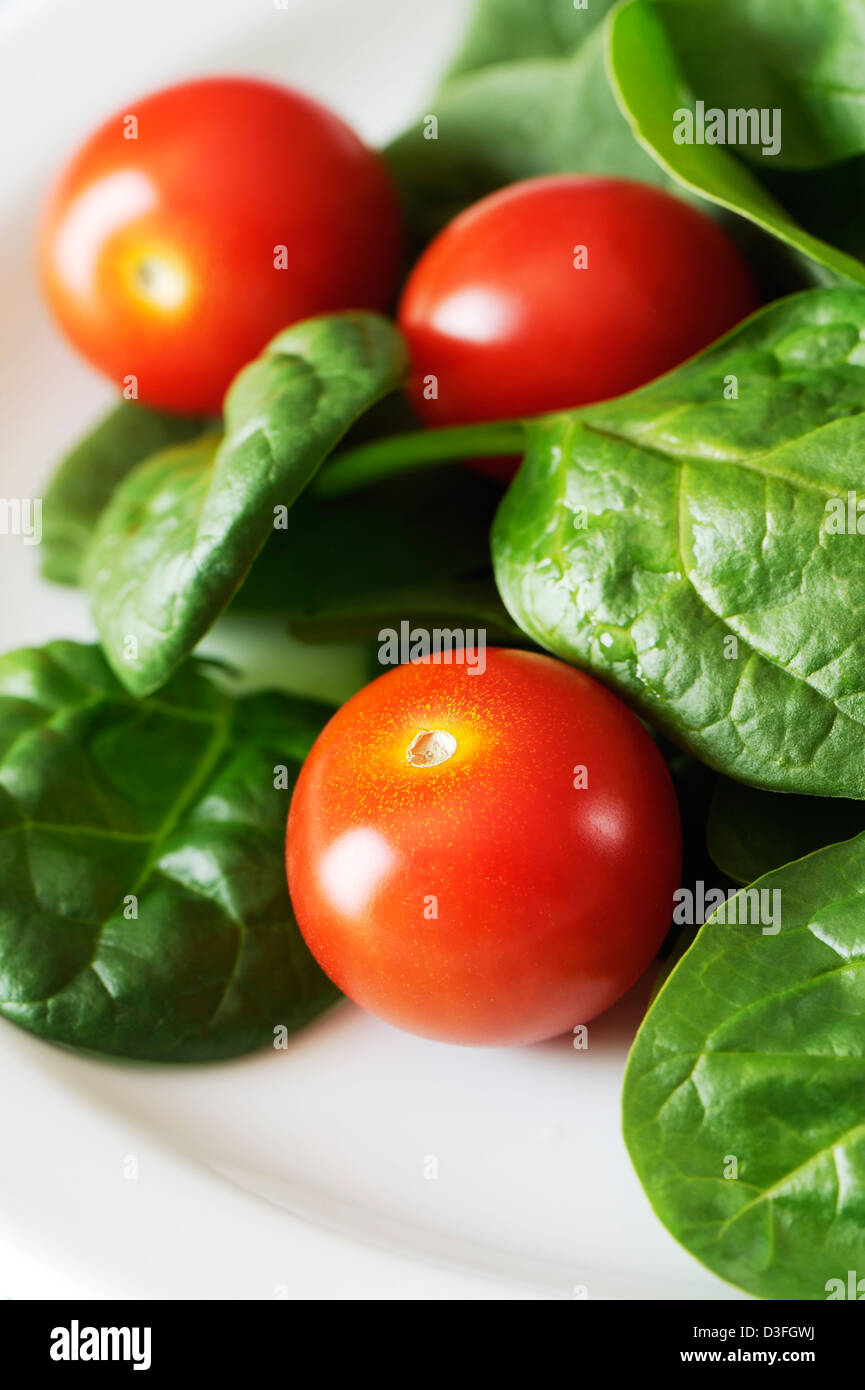 Salade faite de bébés épinards et tomates cerises dans une assiette blanche. Banque D'Images